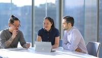 ​Three people sitting at a table looking at a computer and talking.
